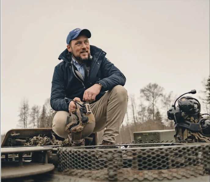 Jo crouching on top of an armoured vehicle, holding a helmet